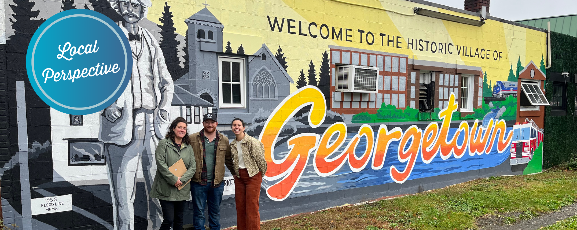 Three people posing in front of a large mural with scenes of Georgetown Connecticut