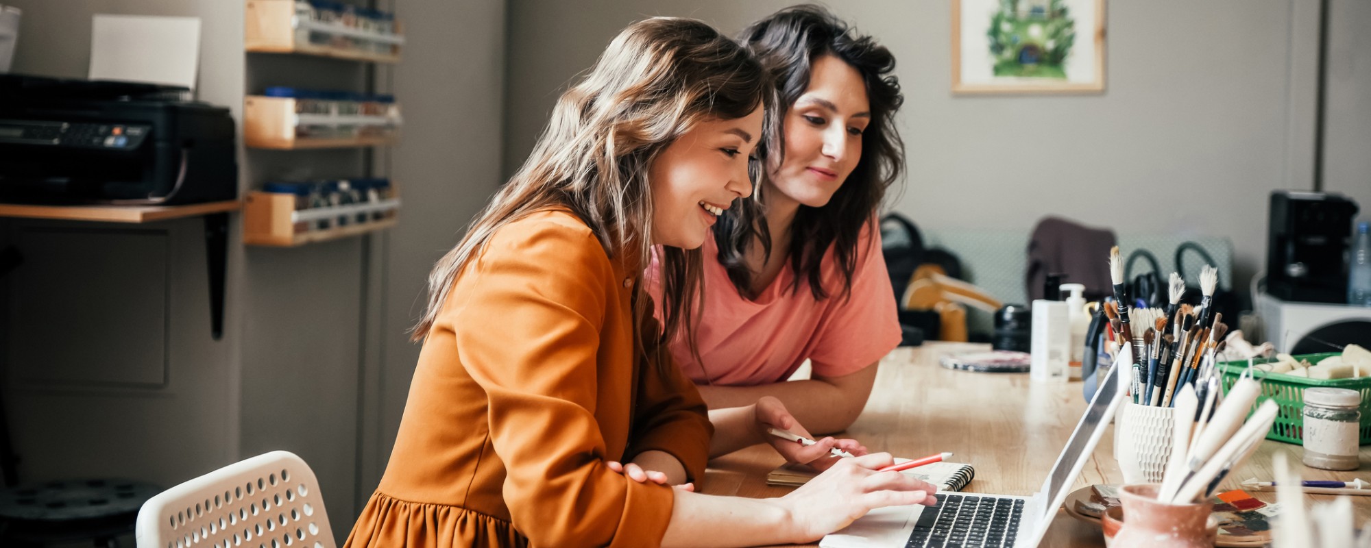 Two woman sitting at a desk looking at a laptop