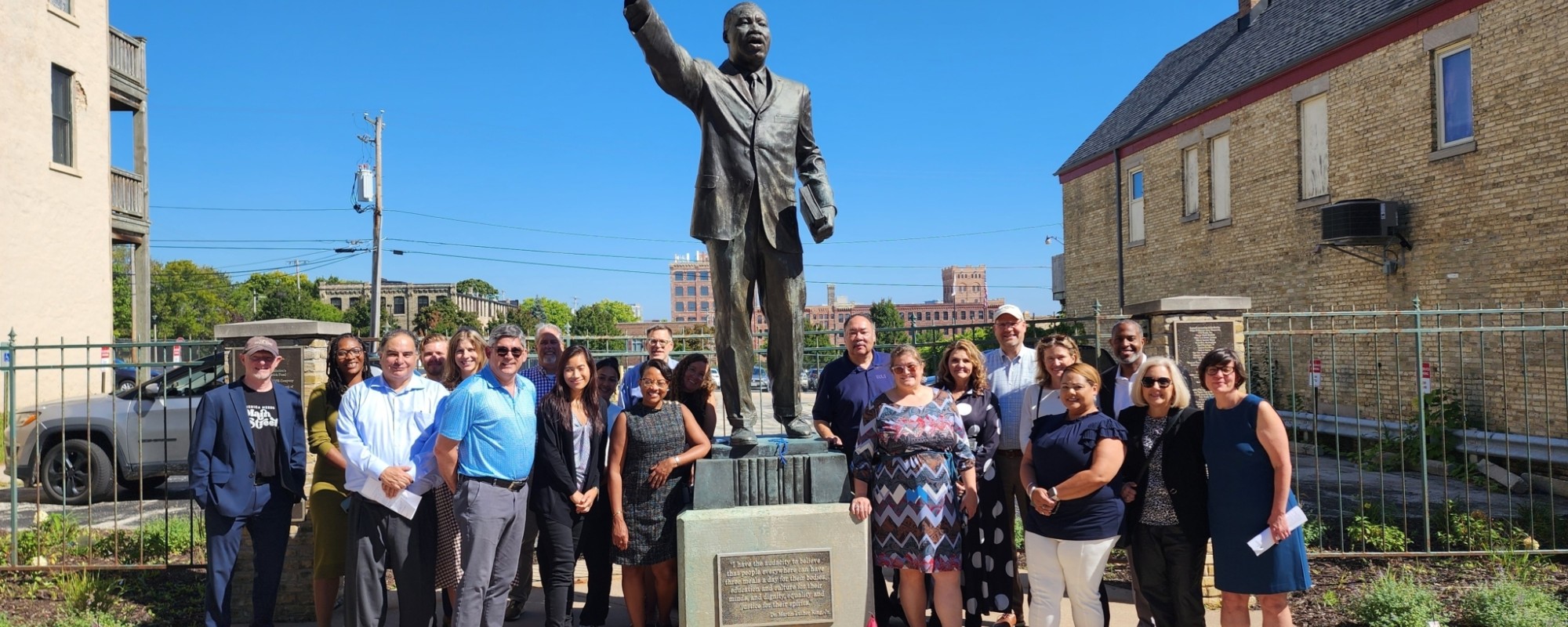 A large group of people poses next to a statue of Martin Luther King Jr. under a clear blue sky