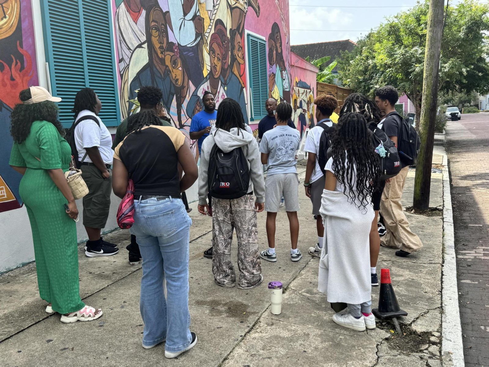 A group of people on a sidewalk in front of a mural