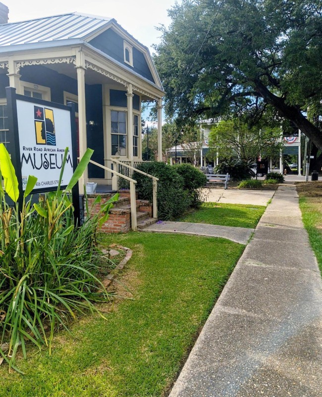 A historic blue building on a sidewalk with green grass and trees