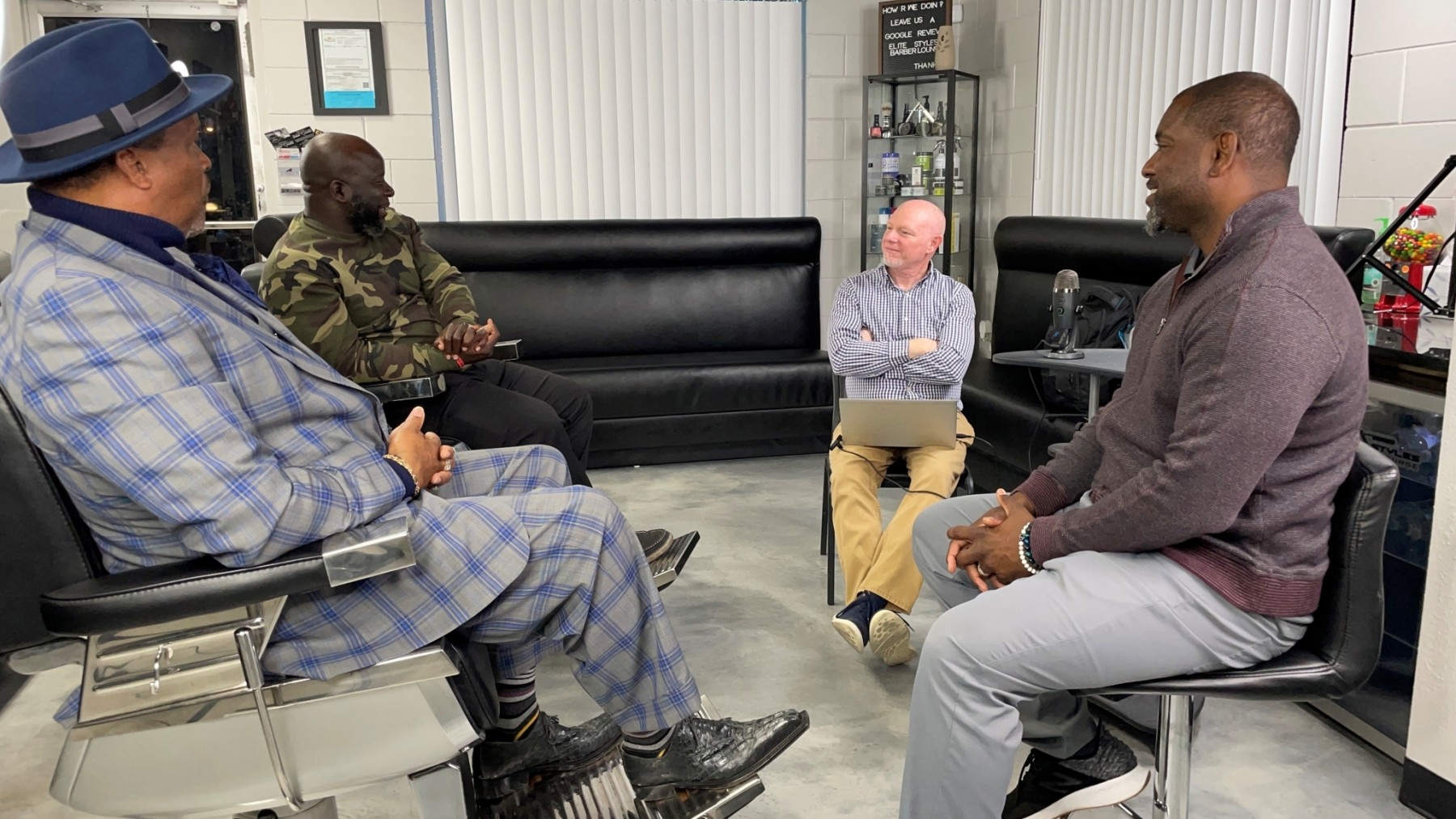 A group of four men sit on chairs in a circle in a barbershop.