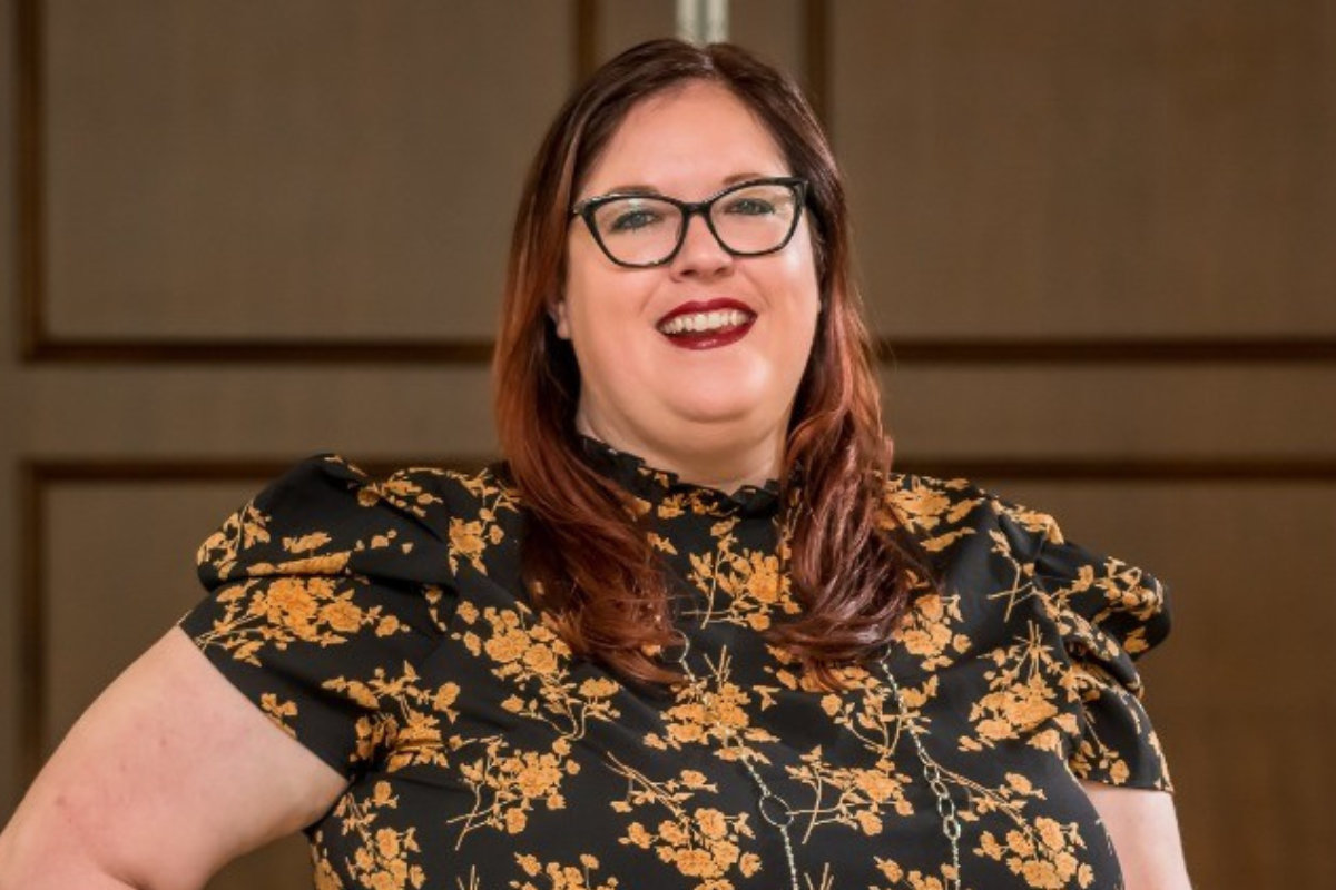Photo of smiling woman with red hair wearing glasses and floral shirt
