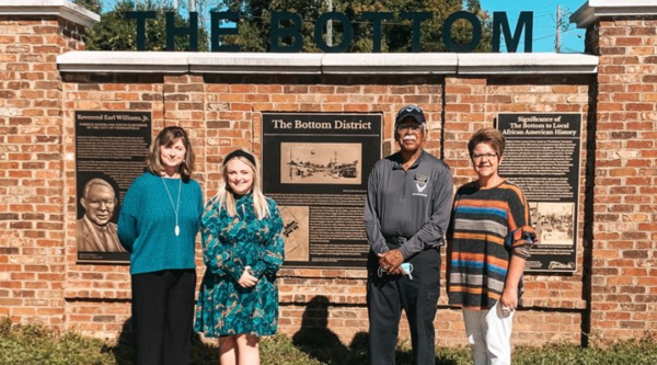 Four people pose in front of a brick wall with interpretive panels
