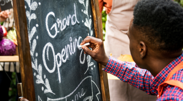 Man writing Grand Opening on a chalkboard outside a small business.