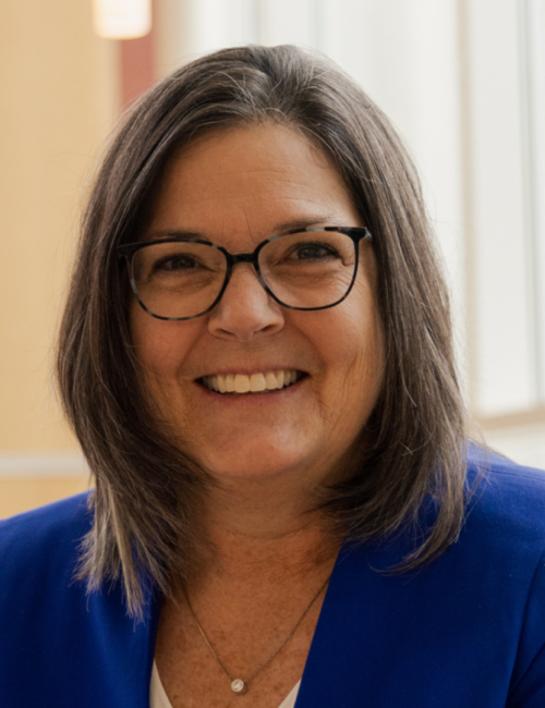 Woman with glasses wearing blue jacket smiles at camera