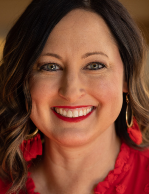 Brunette woman wearing red shirt and red earrings smiles at camera